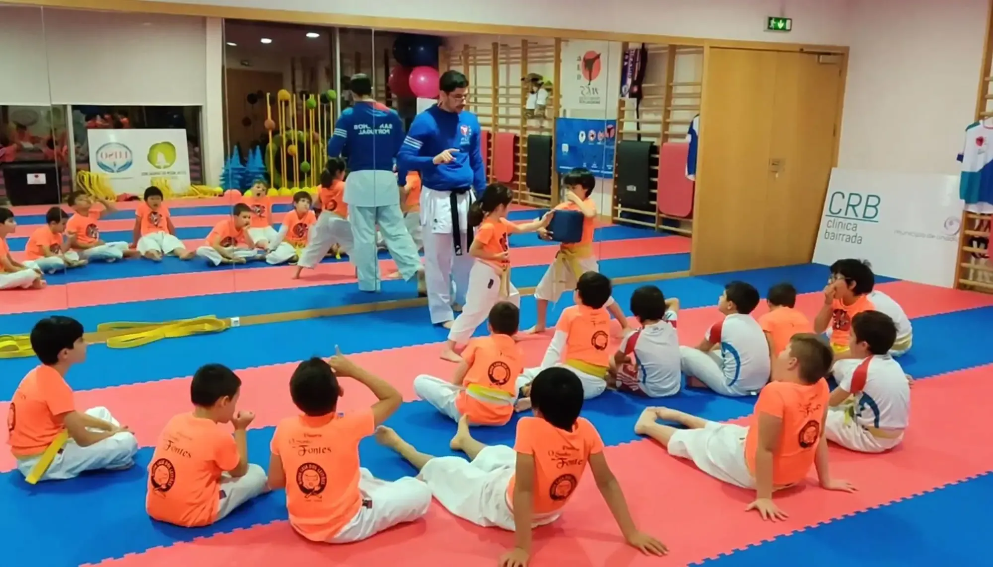 Treino de crianças no dojo, com um exercício de pontapé ao escudo