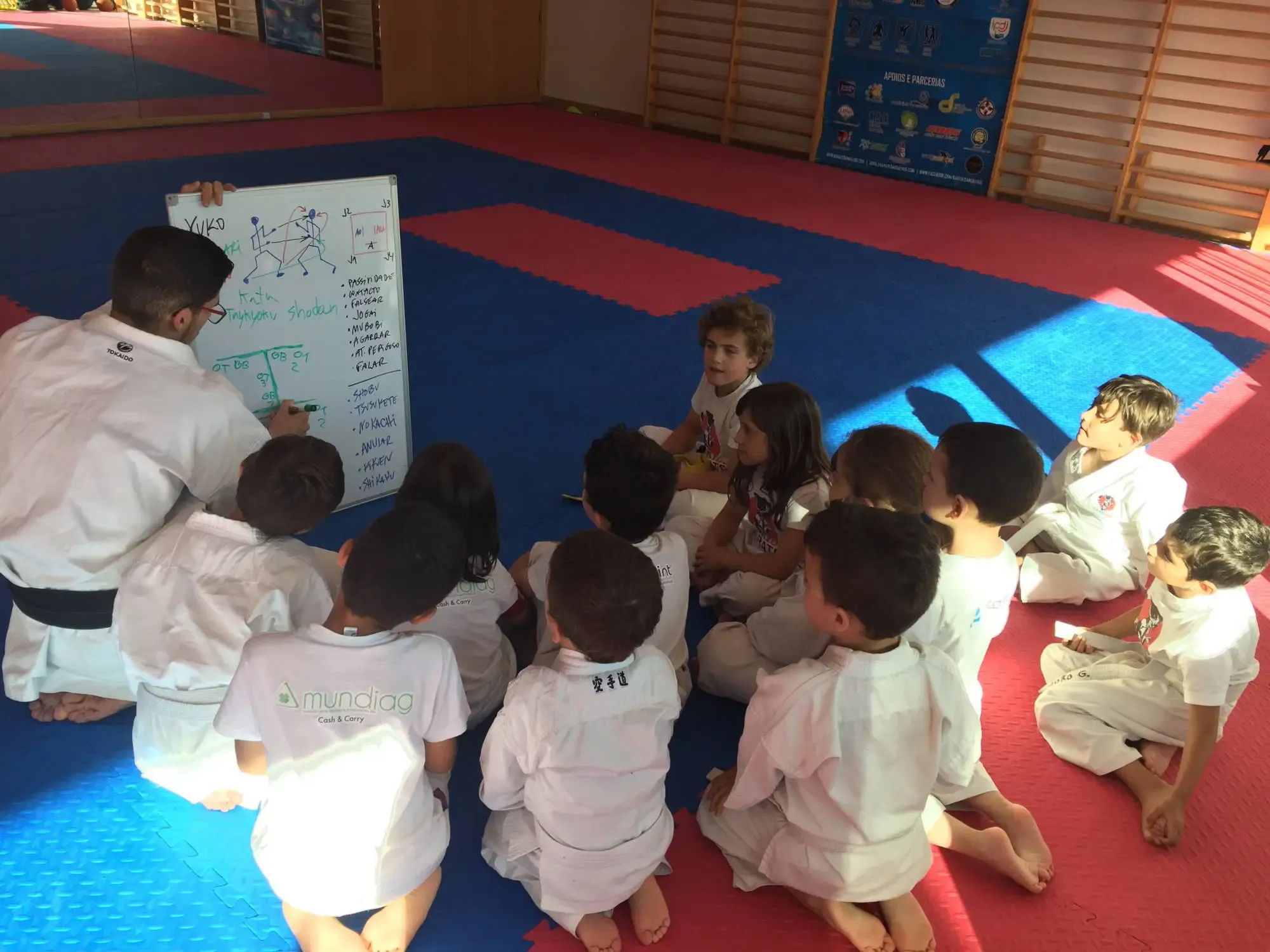 Pedro Miguel explica táticas num quadro branco a crianças sentadas no tatami